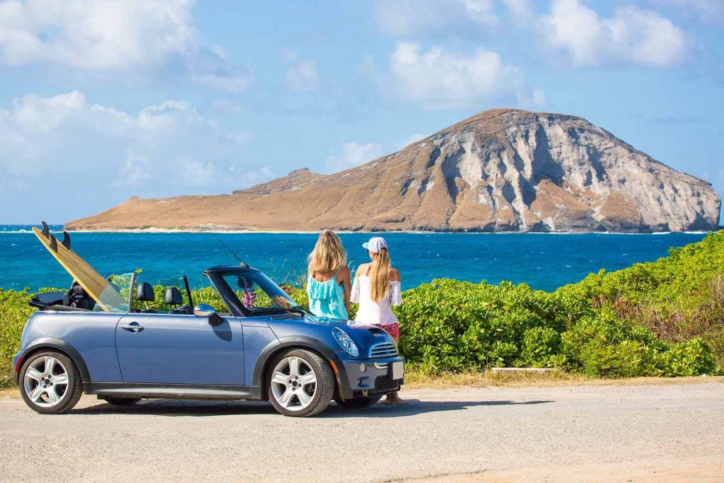 Two people enjoying a scenic coastal view from a parked car in Hawaii