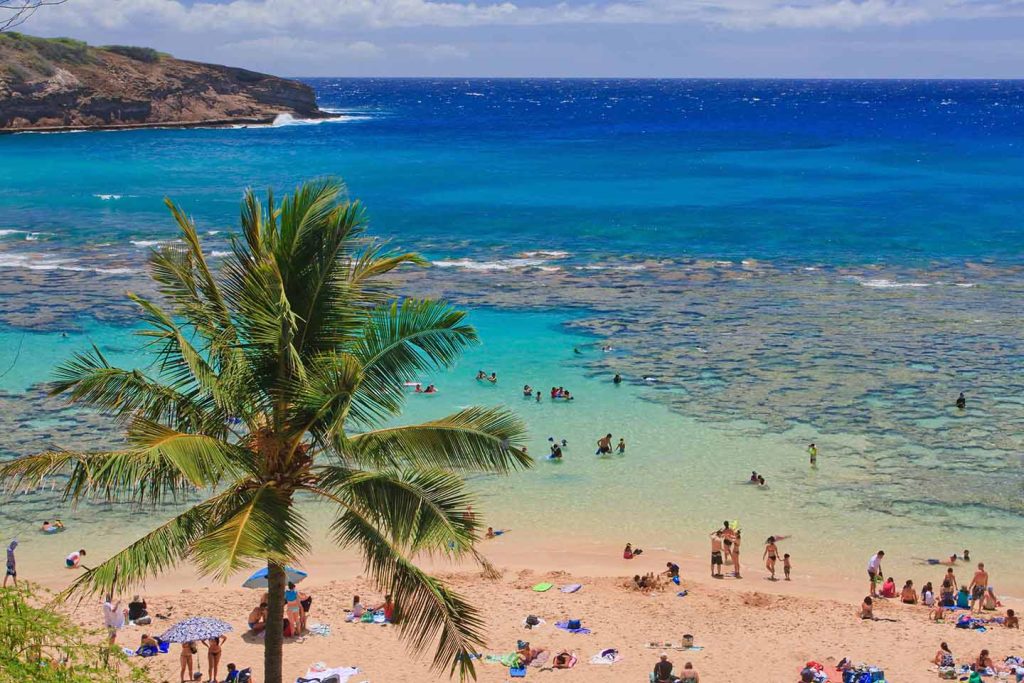 People enjoying a calm beach and lagoon in Hawaii with clear turquoise water